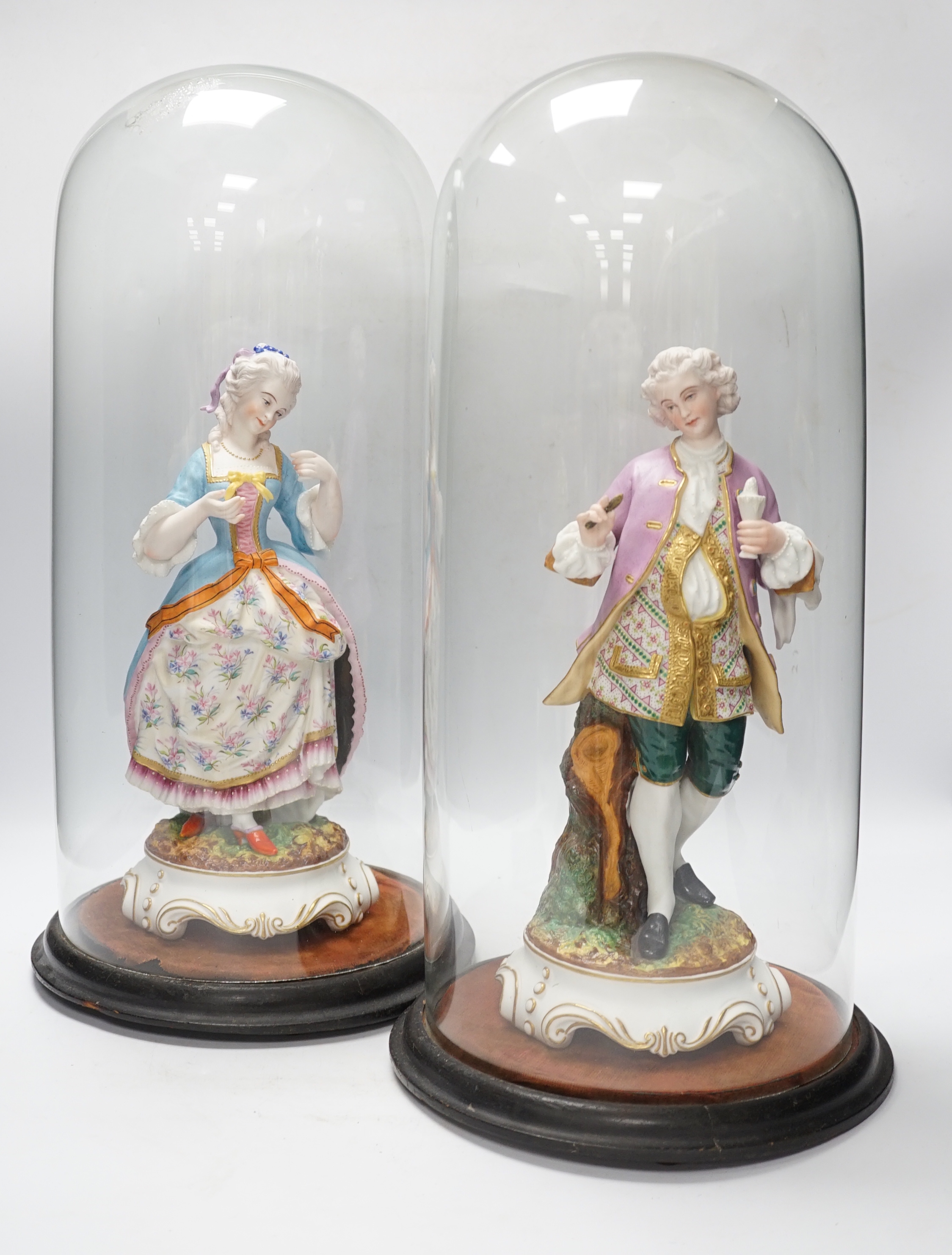 A pair of continental bisque porcelain figures, under glass domes, 48cm overall